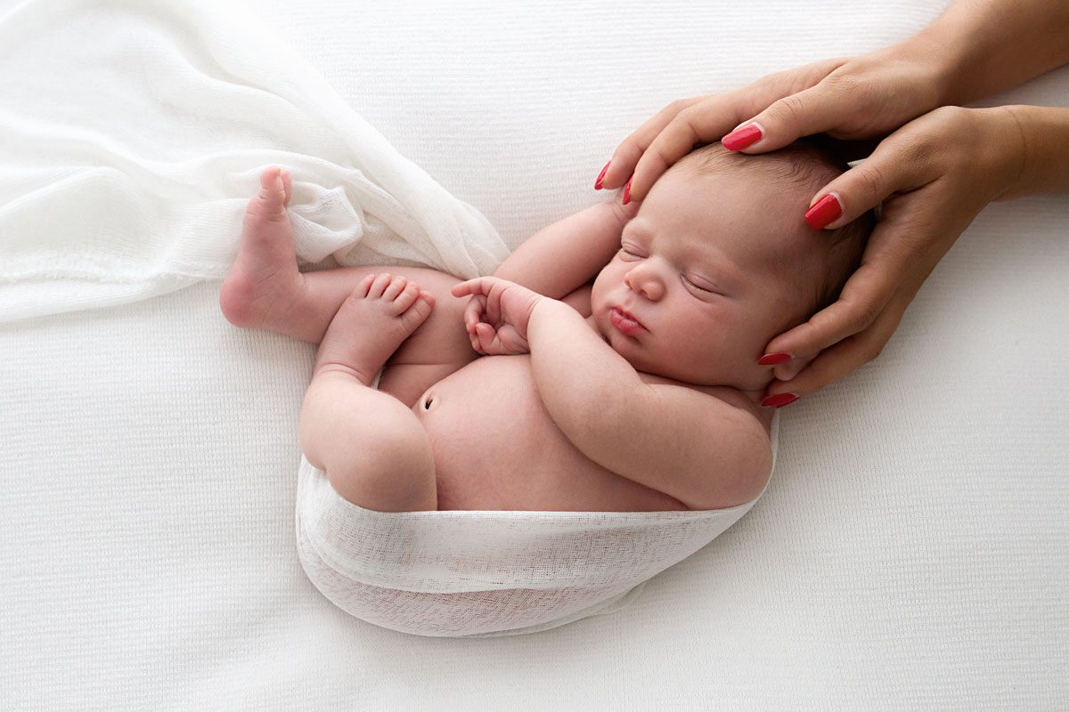 newborn-photographer-london- mum's hands holding baby's head